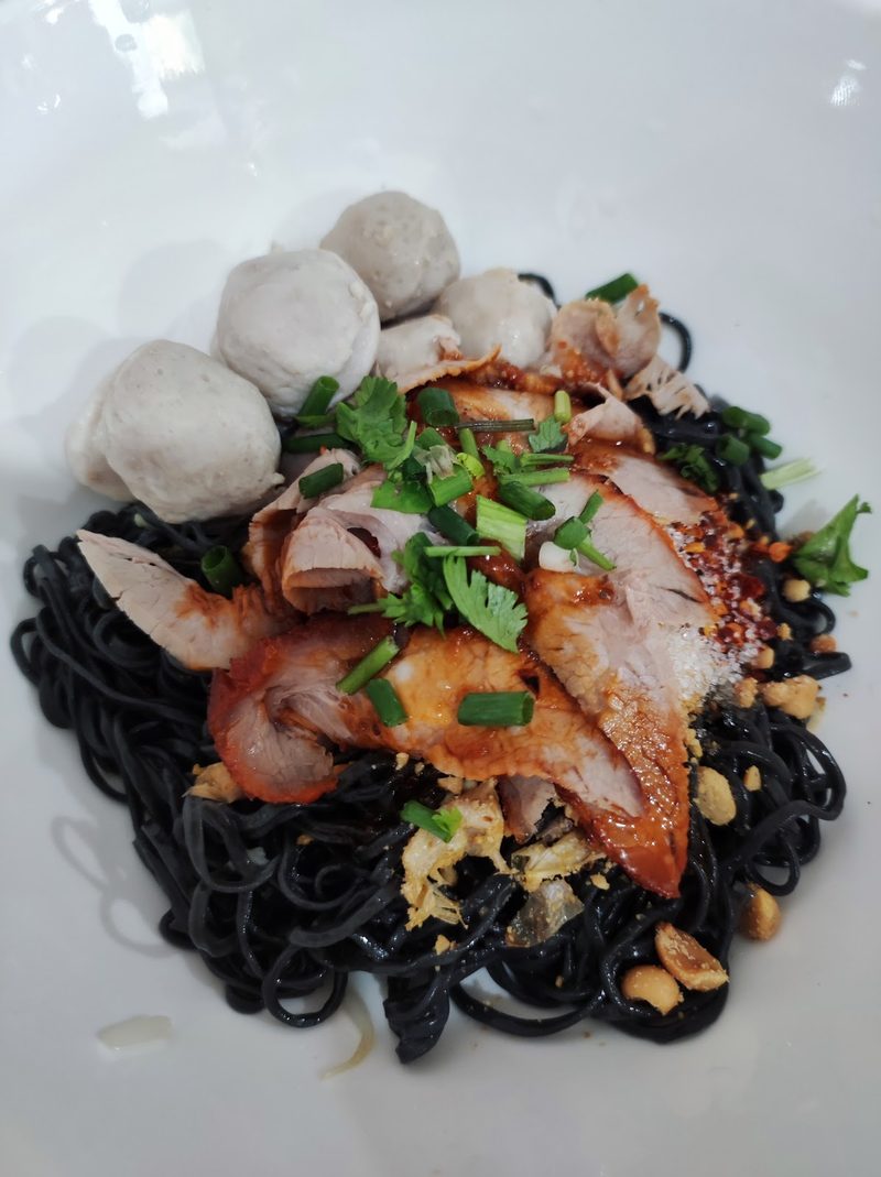 บะหมี่เส้นดำแห้ง โปะหมูแดงและลูกชิ้นหมู โรยผักชีและต้นหอม