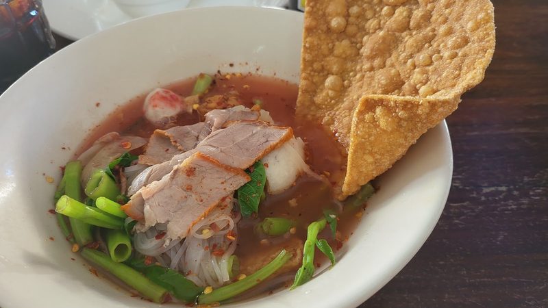 ก๋วยเตี๋ยวน้ำสีชมพู ใส่หมูชิ้น ลูกชิ้น ผักบุ้ง และเกี๊ยวทอดแผ่นใหญ่