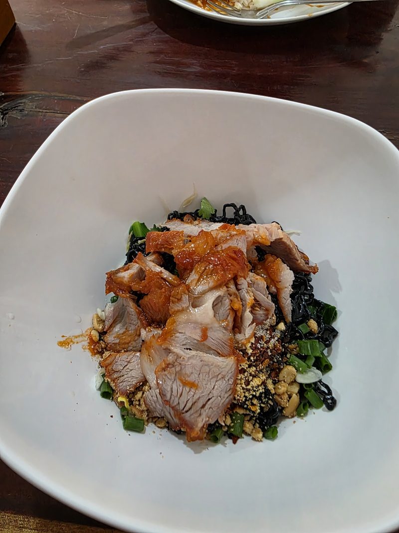 บะหมี่ดำแห้งโปะหมูย่าง ถั่วลิสงป่น และต้นหอม ในชามขาวทรงเหลี่ยม