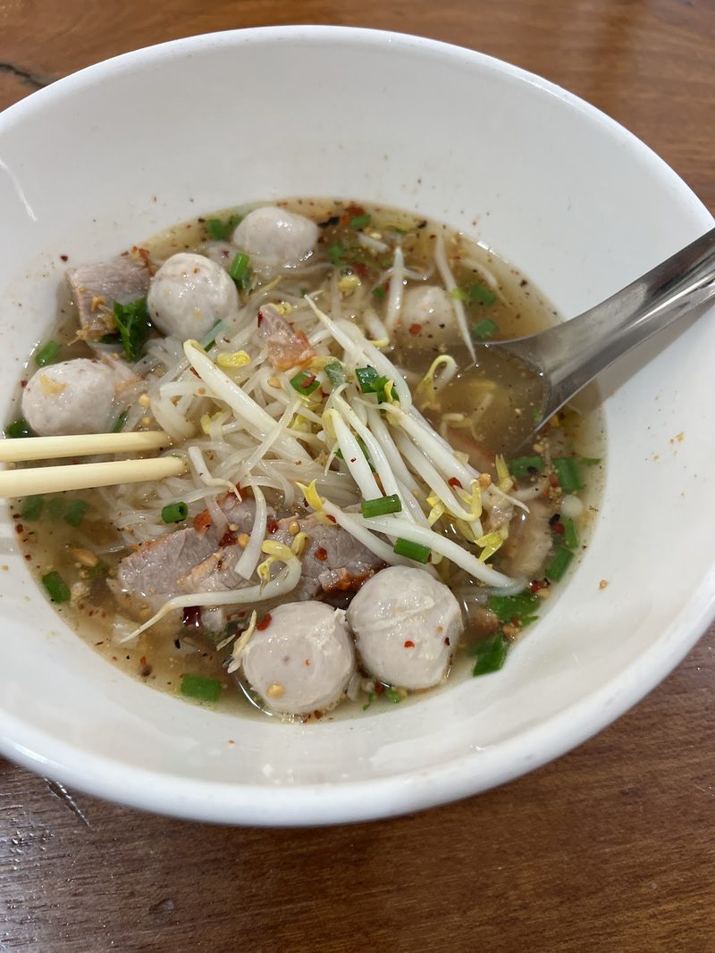 ชามก๋วยเตี๋ยวน้ำซุปใส ลูกชิ้นหมูลอยเต็มชาม โรยถั่วงอกกับต้นหอม มีตะเกียบพาดอยู่
